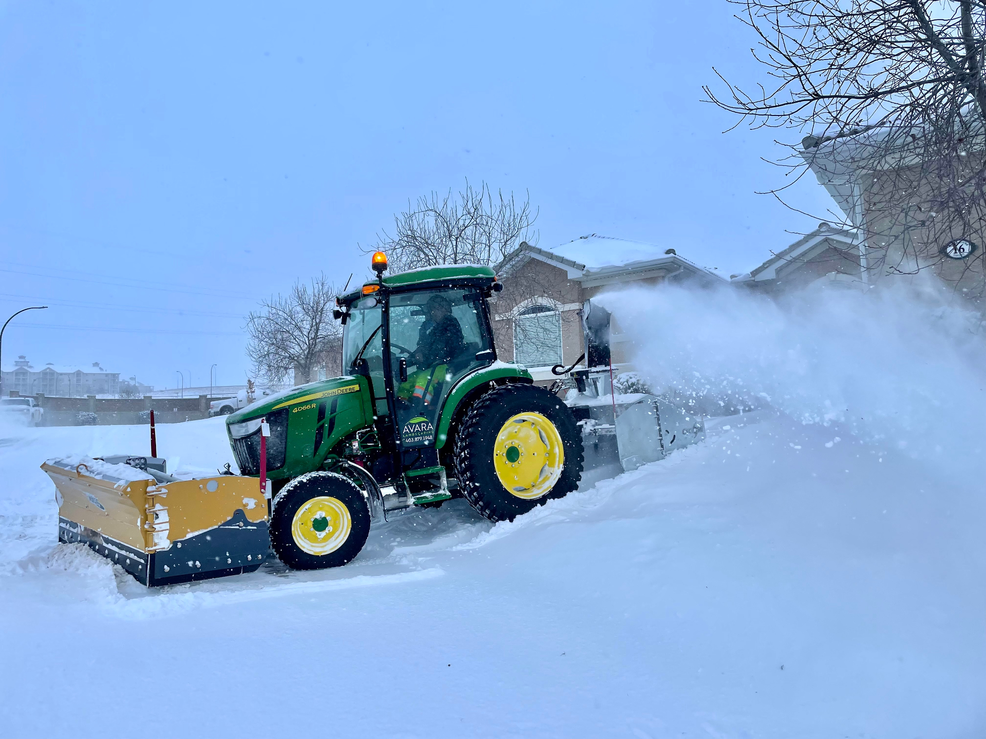 Avara Landscaping John Deere 4066R tractor with plow and snow blower clearing a residential condo complex driveway during a snowstorm