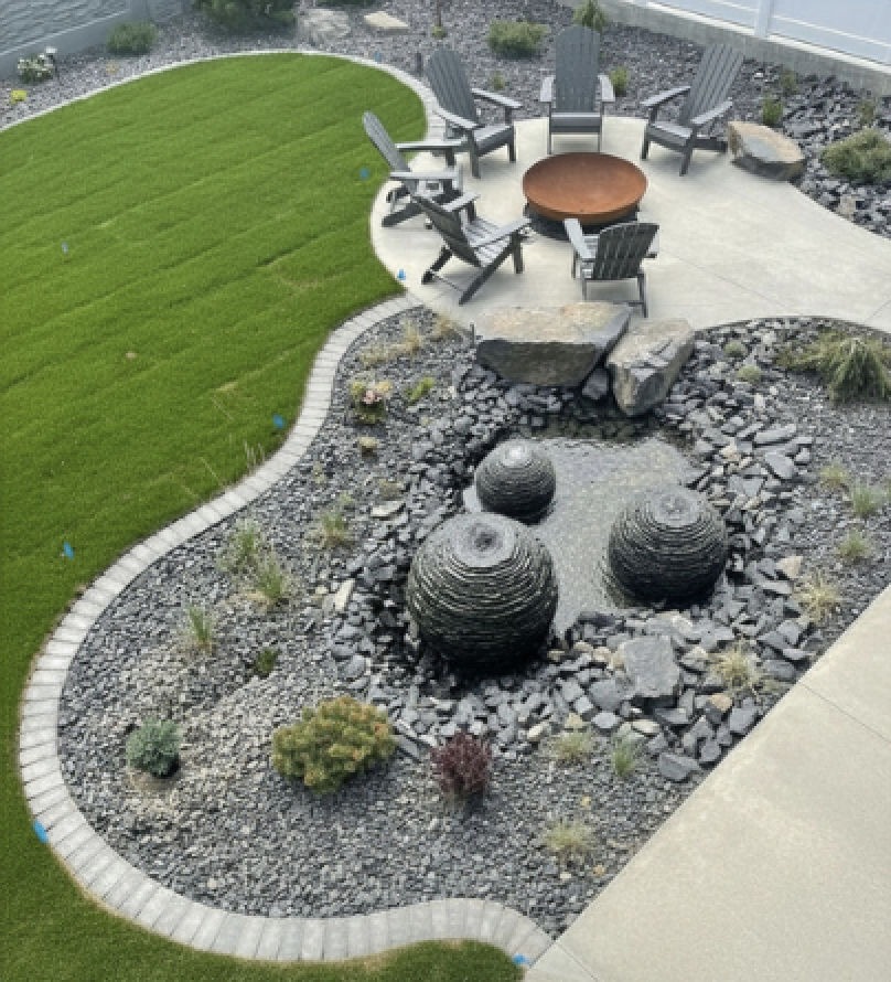 Overhead view of curved paver-edged rock bed with triple basalt sphere water feature, sod lawn, and Adirondack fire pit lounge